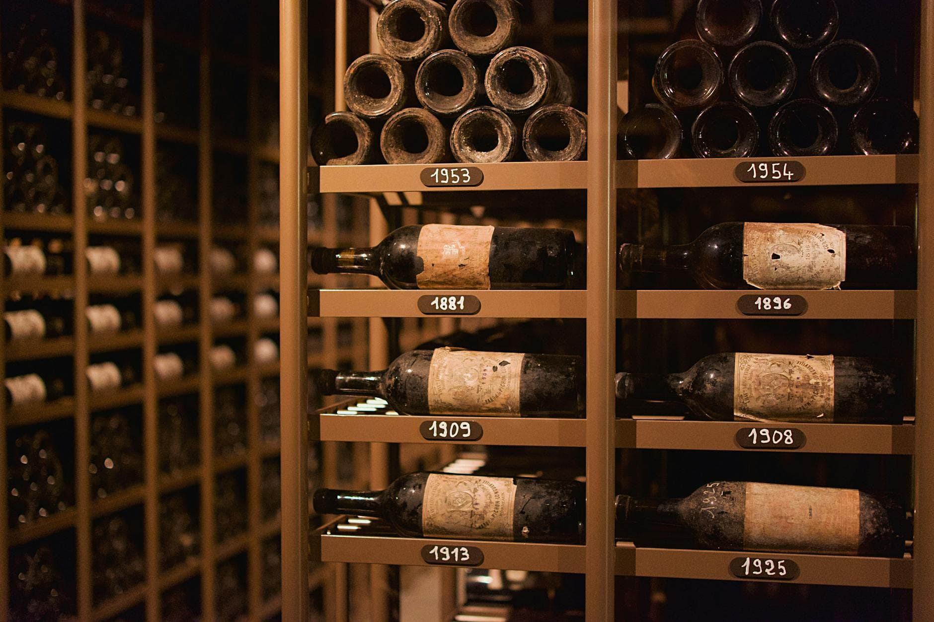 Aged wine bottles stored horizontally in a wooden cellar rack, dust on the bottles indicating long-term cellaring