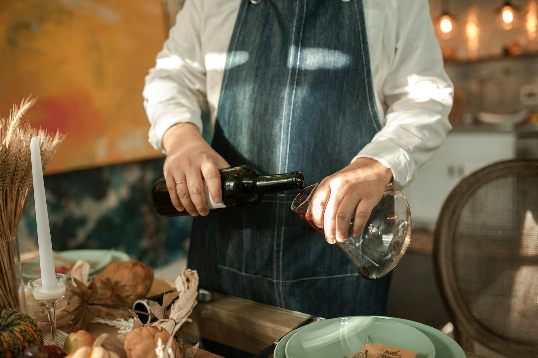 A person decanting red wine into a glass decanter at a dinner table with warm candlelight