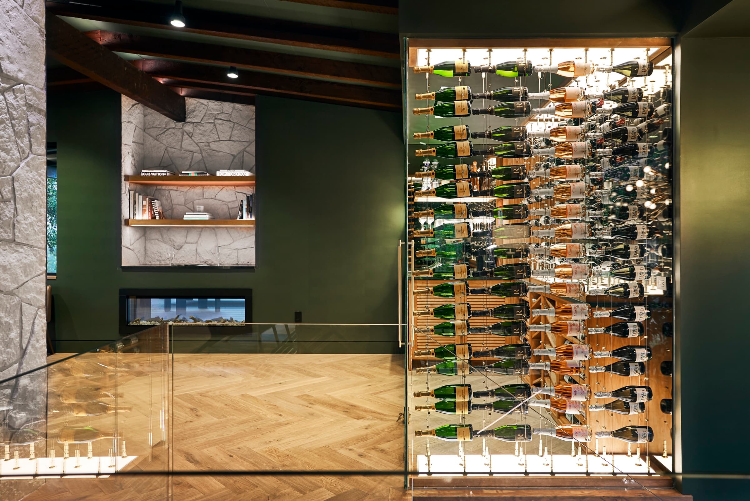 A wide angle of the Bijou Wine Cellars showroom in Westlake Hills, showing the stone feature wall and fireplace on the left and the cable-suspension wine cellar on the right, framed by exposed wood ceiling beams