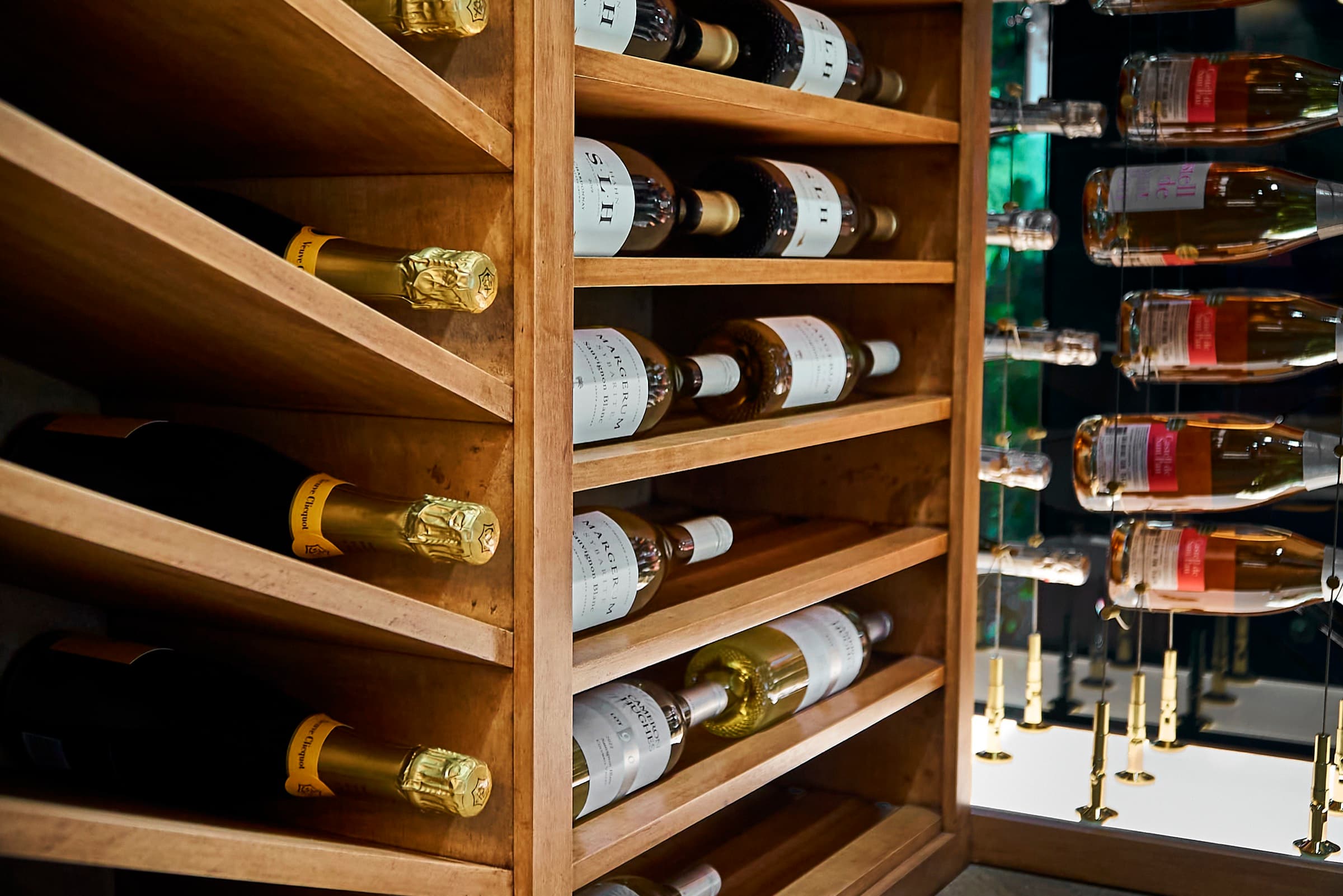 Detail of the Bijou house wine cellar showing the transition from hand-crafted wood slant racking holding Champagne and white wines to the cable-suspension display wall holding rosé sparklings